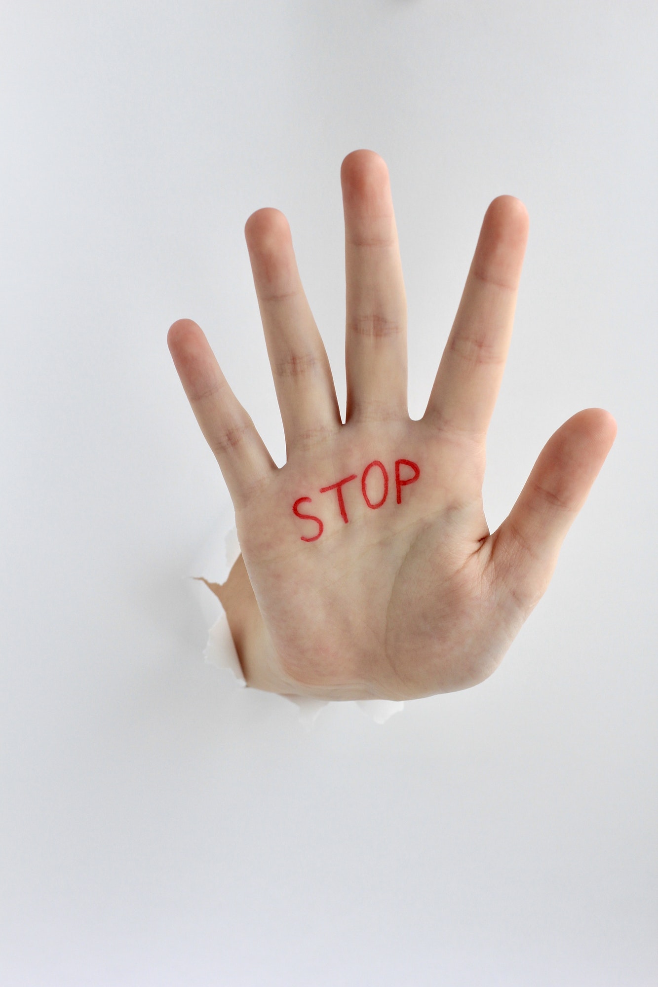 Hand with text stop written on the palm showing stop gesture through a hole in paper.